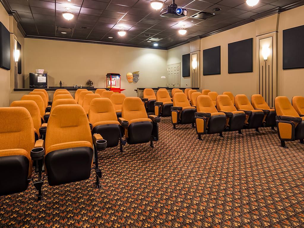 An empty movie theater with orange seats and a projector screen.