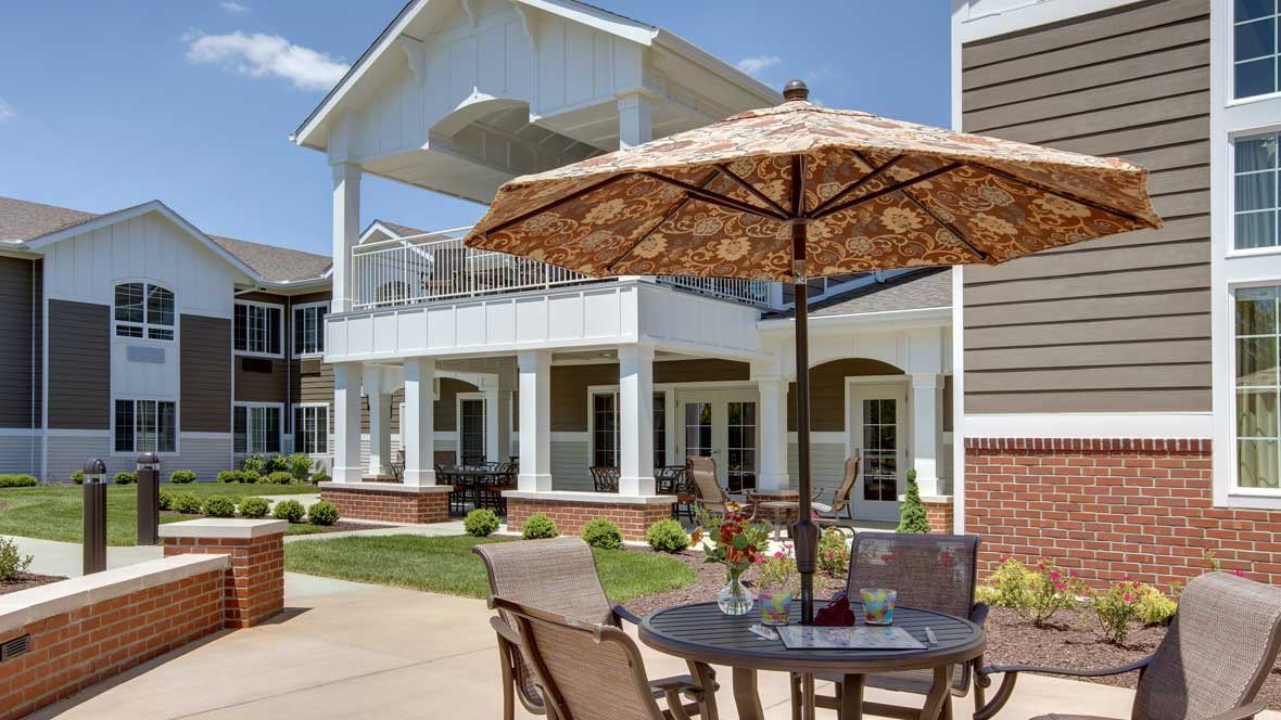 A sunny patio with a table and chairs under an umbrella, in front of a modern building.