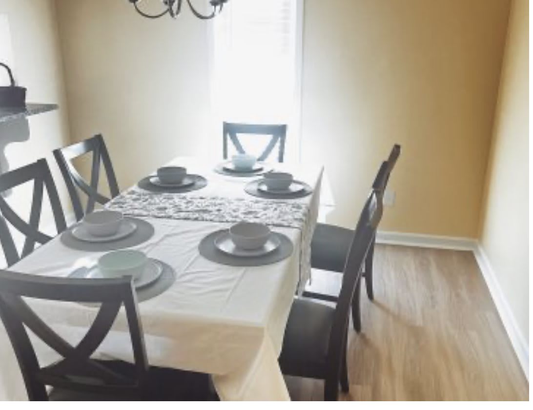 A dining room with a neatly set table, featuring a white tablecloth, black chairs, and matching dishware.