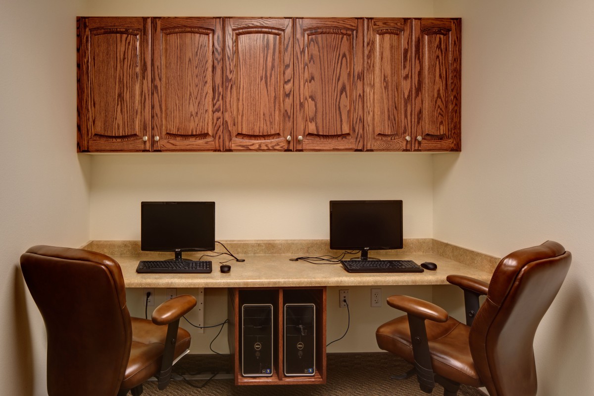 A small office workspace with two computer stations, complete with monitors and chairs, set beneath wooden cabinets.