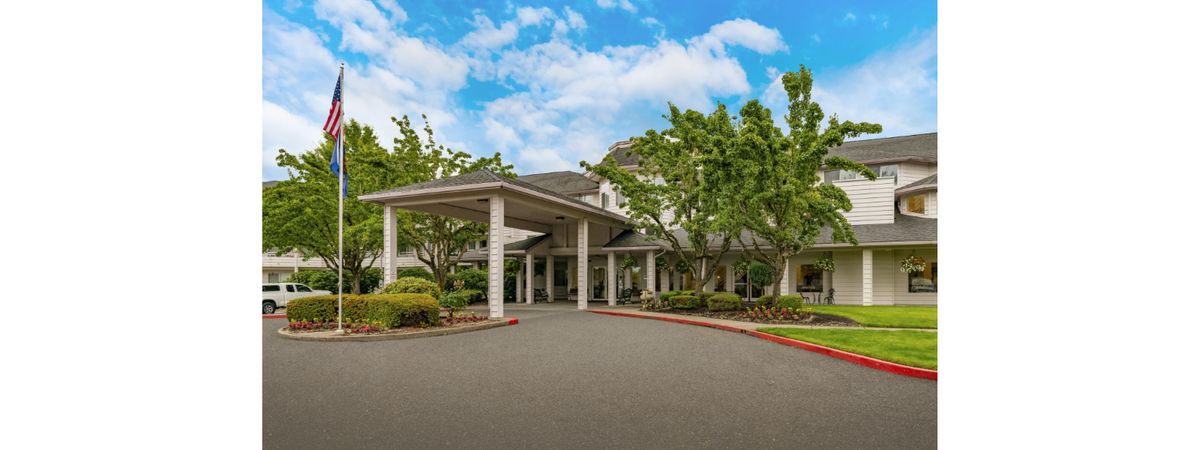 A large building with a columned entrance and surrounding greenery under a partly cloudy sky.