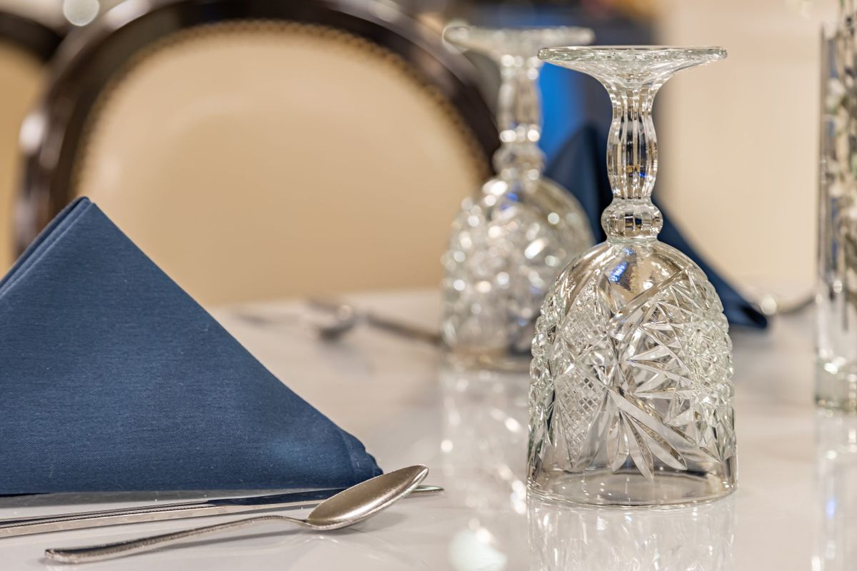 An elegantly set dining table with folded blue napkins and intricately designed glassware.