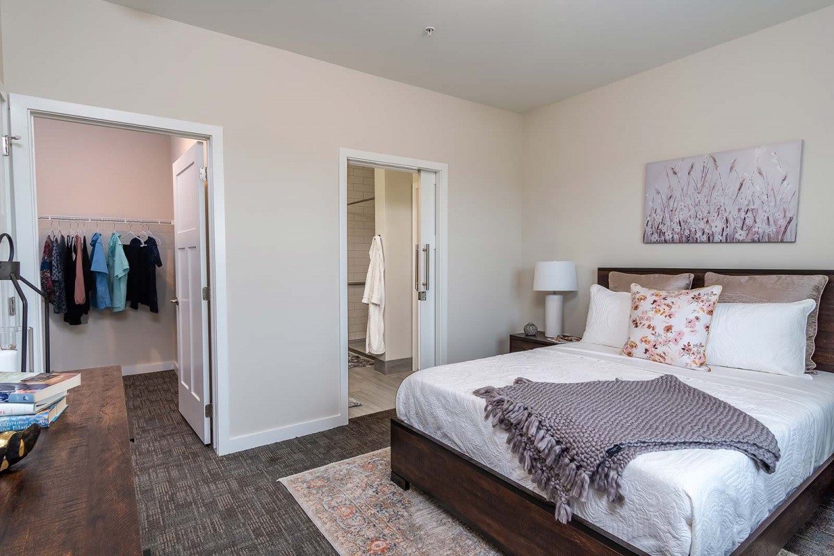 A modern bedroom with a neatly made bed, bedside lamp, and wall decor.
