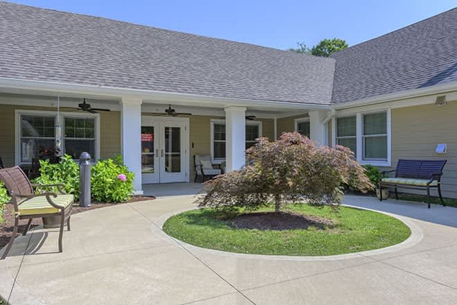 A welcoming entrance to a residential building with landscaped greenery and a curved sidewalk.
