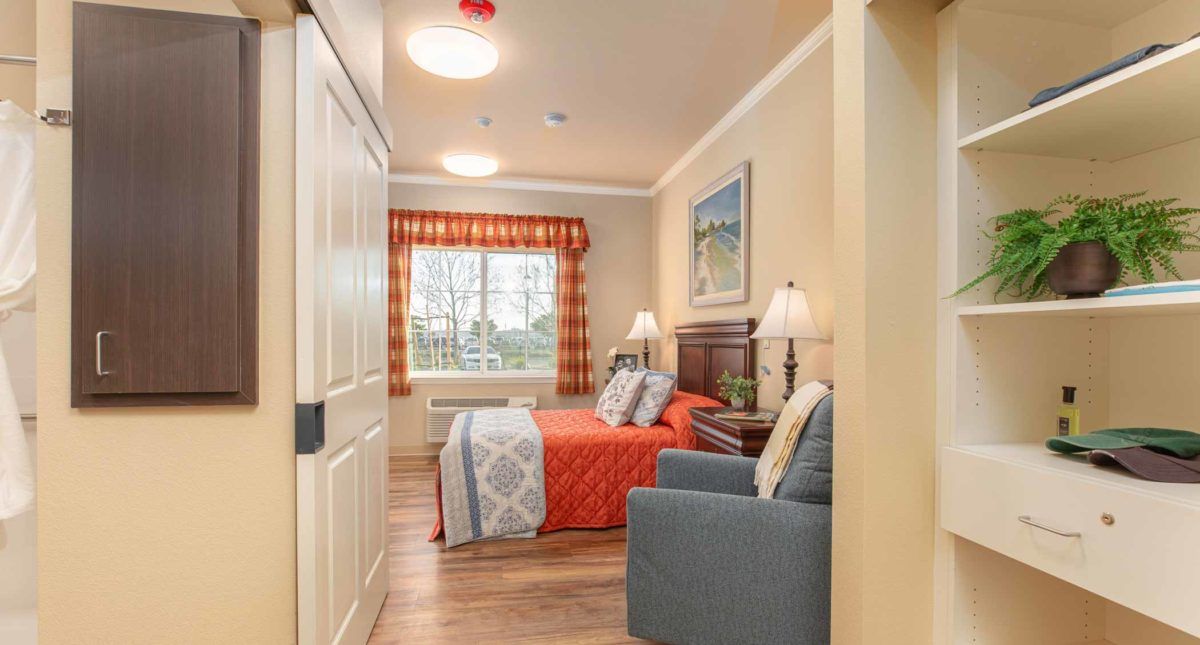 A cozy bedroom featuring a bed with red bedding, two bedside lamps, and a window with patterned curtains.