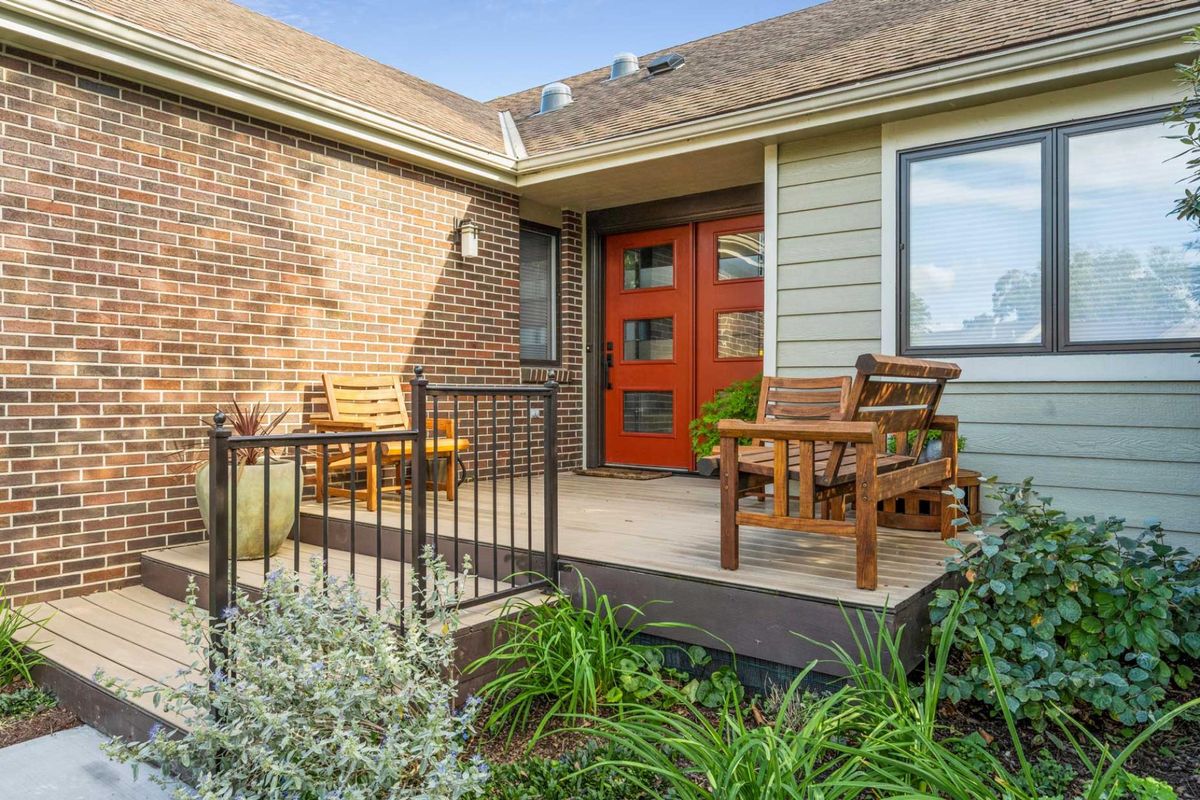 A modern house entrance featuring a front porch with wooden furniture and brick exterior.
