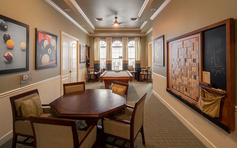 A well-furnished room with tables and chairs, decorated with artwork and featuring large windows.