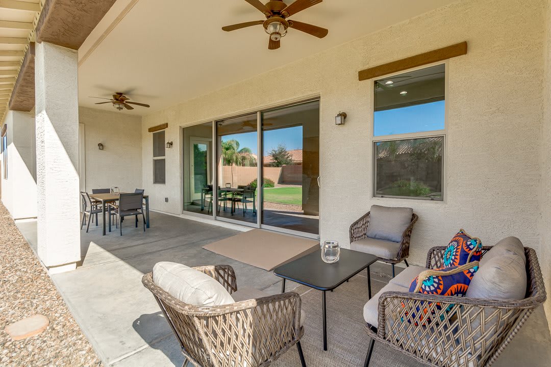 A cozy patio area featuring wicker furniture and ceiling fans, overlooking a backyard through sliding glass doors.