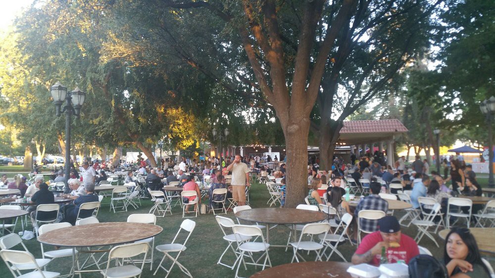 A large group of people gathered outdoors with tables and chairs under trees.