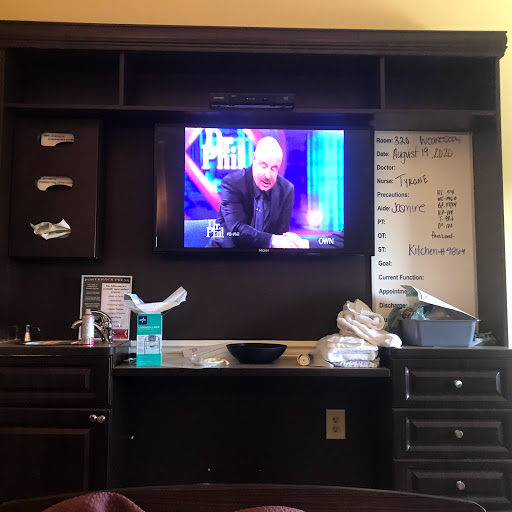 A hotel room setup featuring a television mounted on a wall unit with various personal items and drinks nearby.
