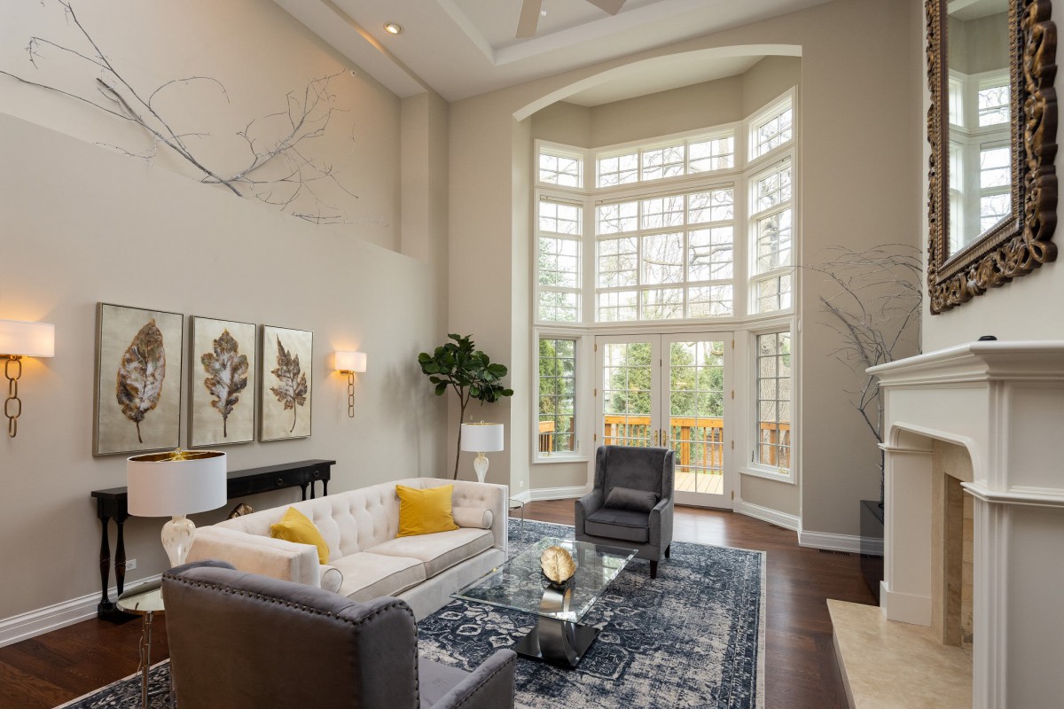 A modern living room with high ceilings and large windows, featuring a sofa, armchairs, and a coffee table.