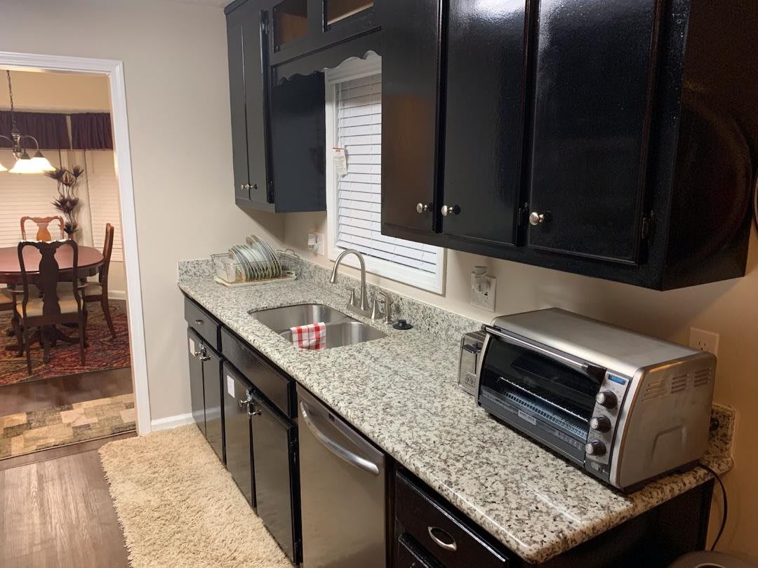 A modern kitchen with granite countertops and dark cabinets, featuring a sink and a toaster oven.