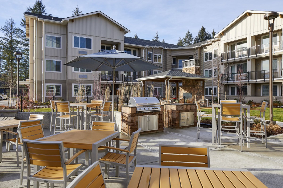 A modern apartment complex with an outdoor patio featuring seating and a grill area.