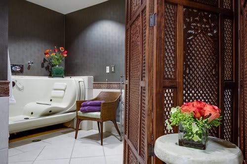 A serene spa setting featuring a comfortable chair, a luxurious tub, and vibrant floral arrangements.
