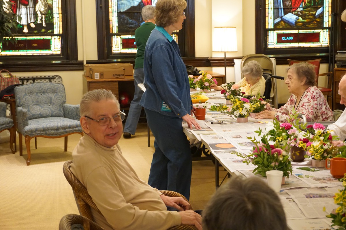 A group of seniors gathered around a table for a social event in a warmly lit room.