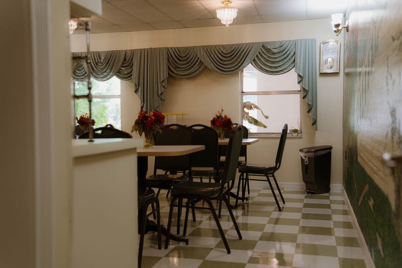 A cozy dining room with checkered flooring, adorned with elegant curtains and flower arrangements on the tables.
