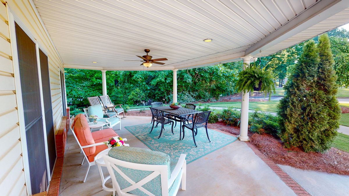 A cozy outdoor patio with a dining set and ceiling fan, overlooking a lush garden.