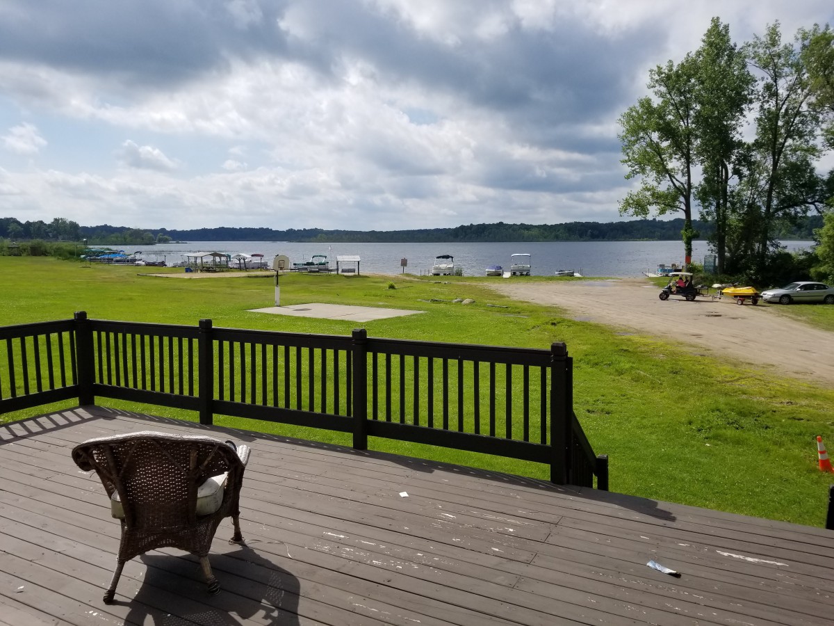 A scenic lakeside view with a deck, chairs, and a cloudy sky.