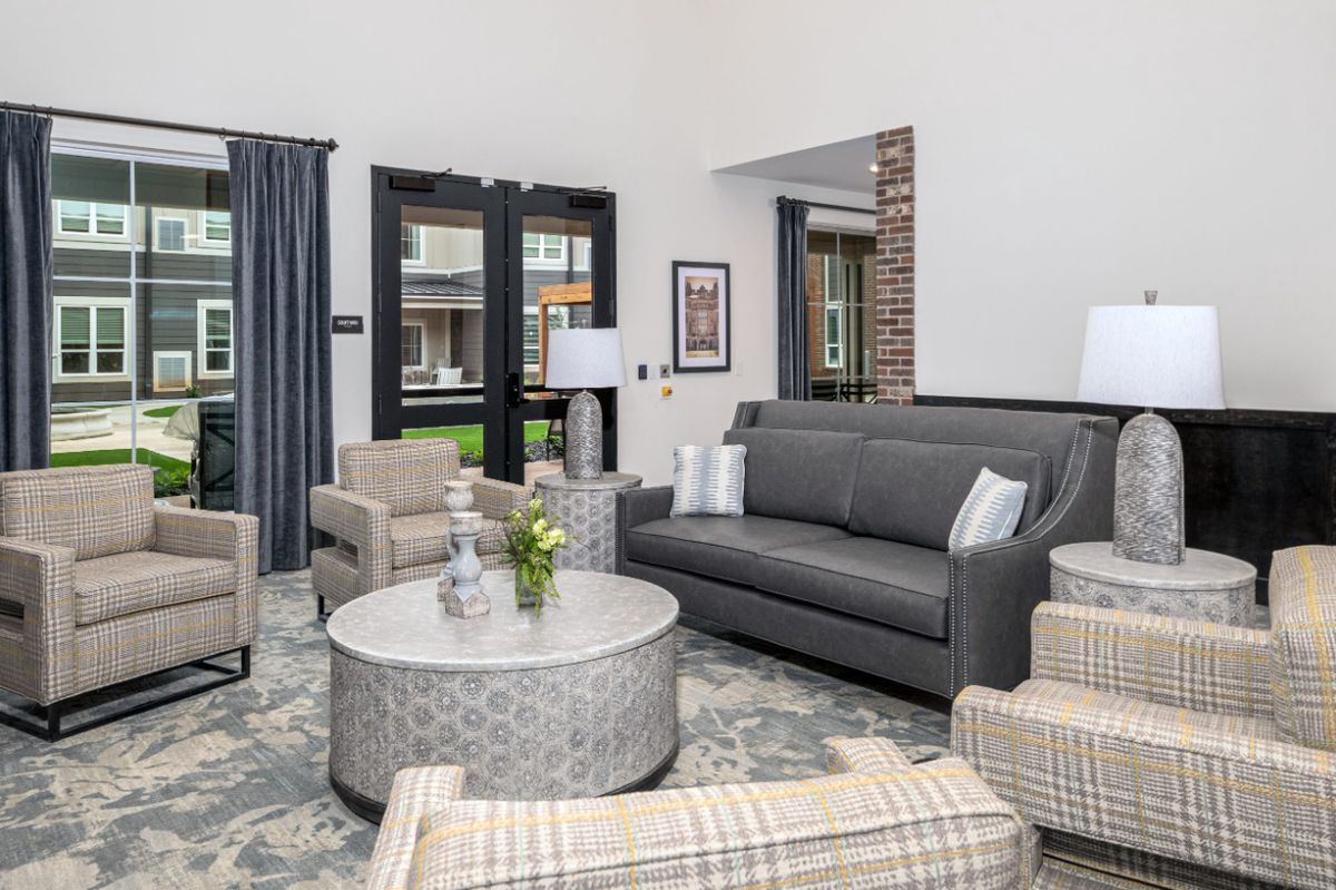 A modern living room featuring a gray sofa, patterned armchairs, a stylish coffee table, and decorative elements like curtains and a vase with flowers.