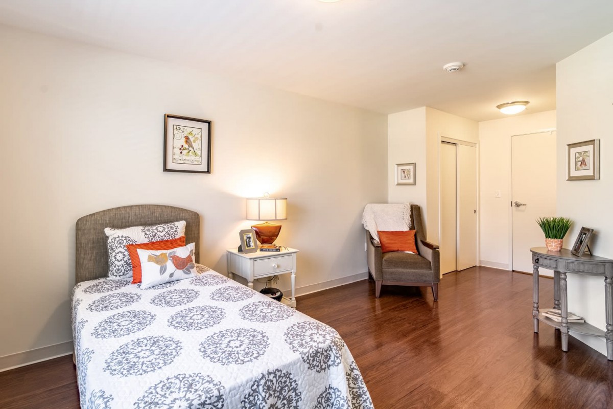 A cozy bedroom with a patterned bedspread, bedside lamp, and comfortable chair.