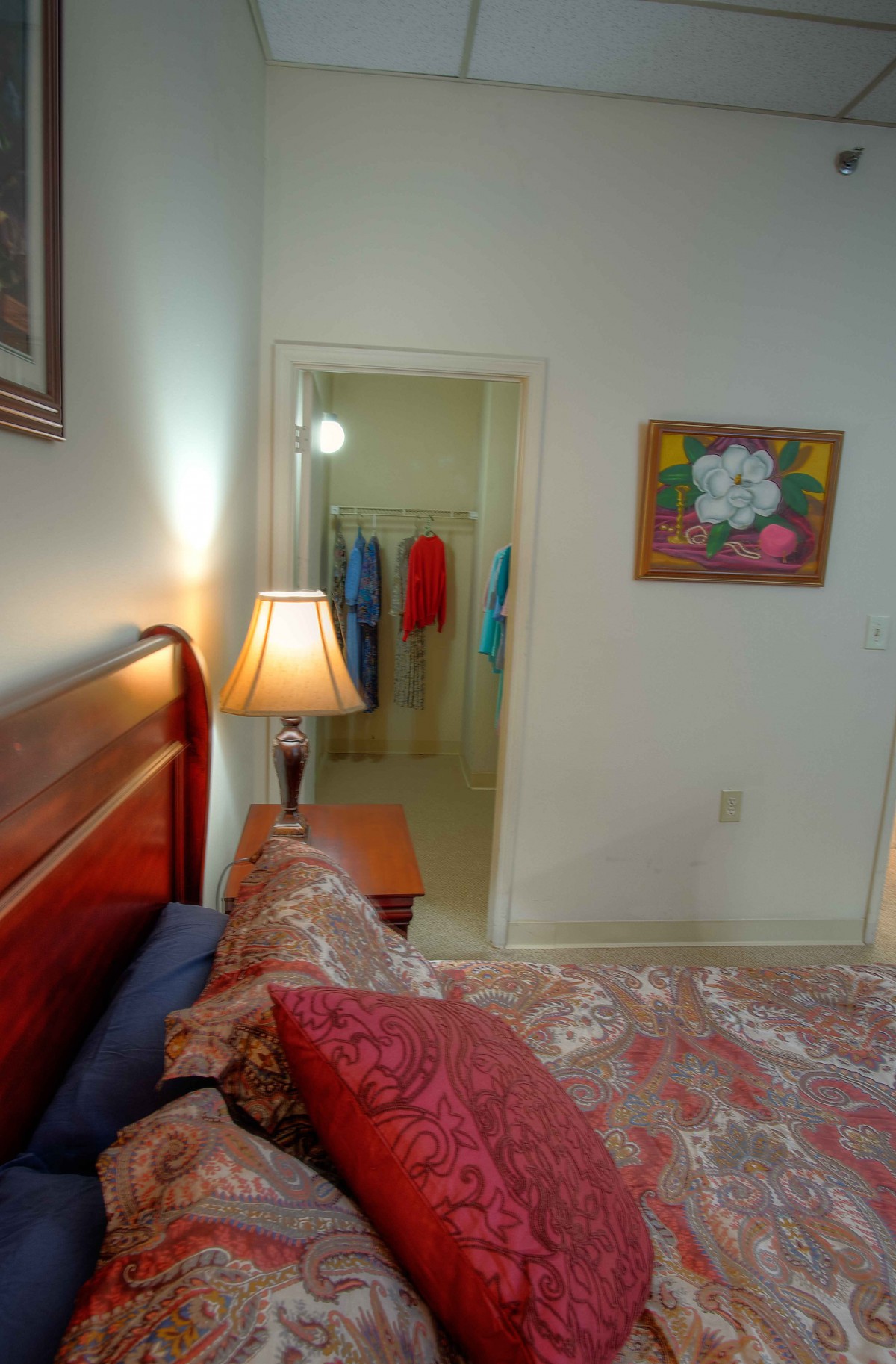 A cozy bedroom with a wooden bed, a lamp on the side table, and an open view into a closet.