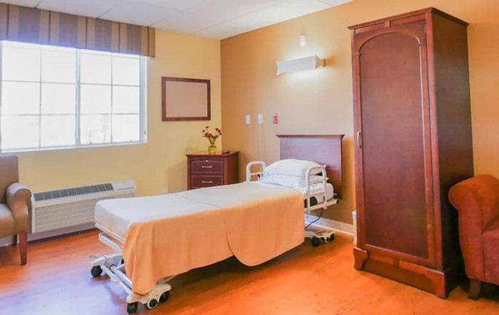 A well-lit hospital room with a single bed and wooden furniture.