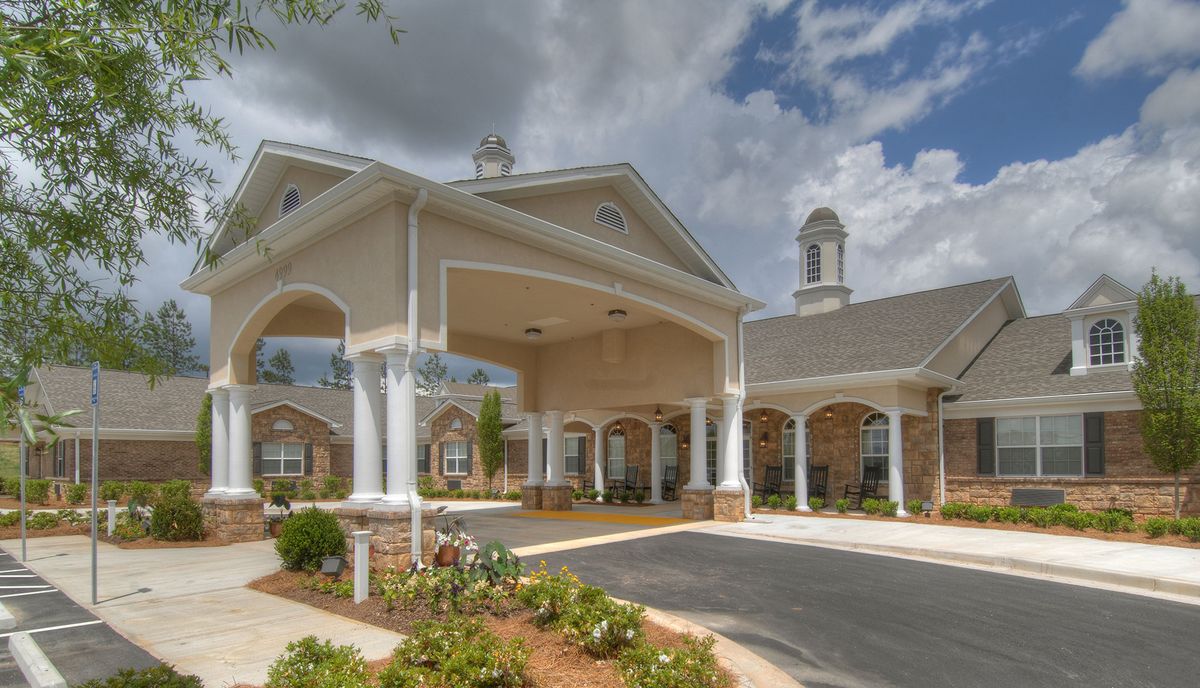 A grand entrance with columns and a driveway leading to a building under a cloudy sky.