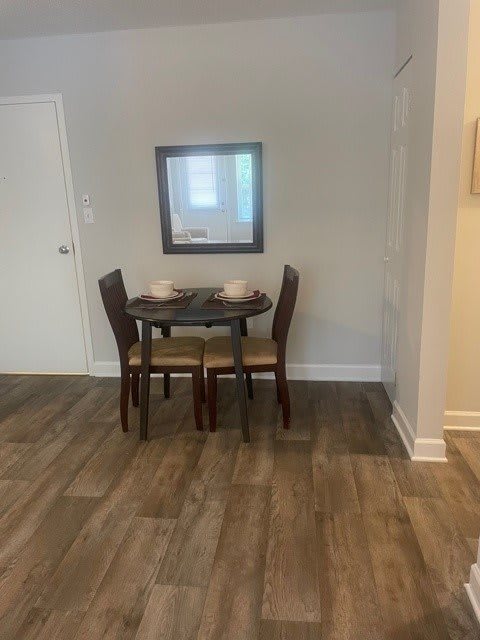 A minimalist dining area with a wooden table and four chairs, complemented by a wall-mounted mirror.