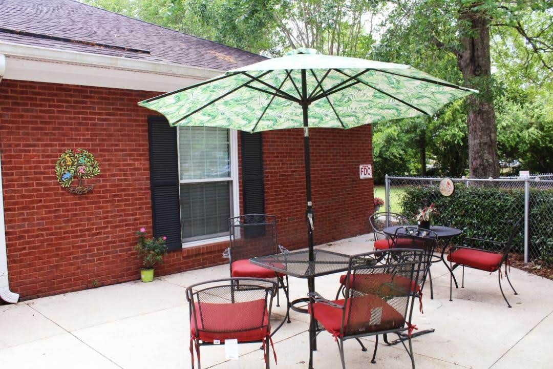 A cozy patio setup with a table and red-cushioned chairs under a green umbrella, set against a brick house backdrop.
