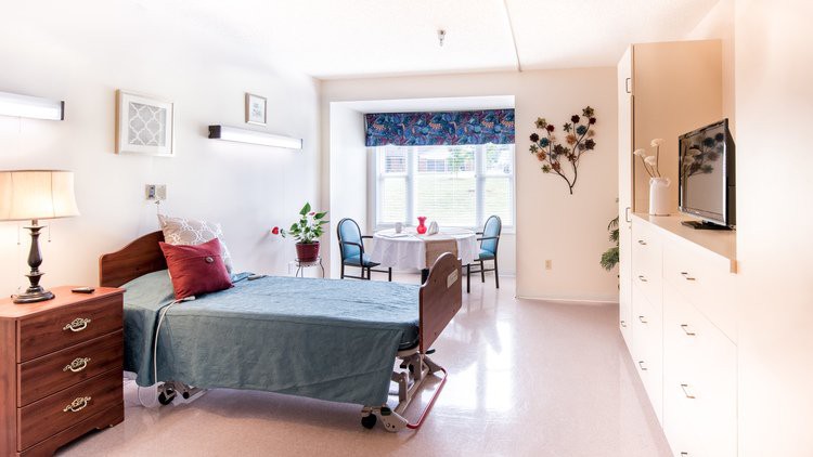A well-lit hospital room featuring a patient bed, chairs, and decorative elements.