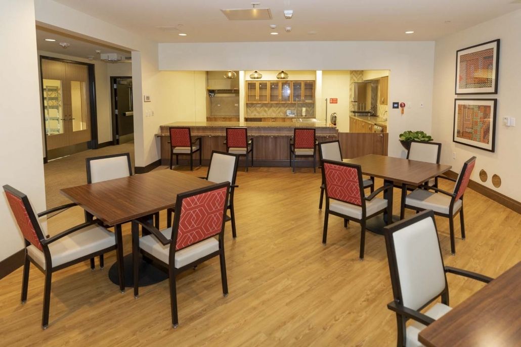 A modern dining area with multiple tables and chairs, featuring warm lighting and wooden flooring.