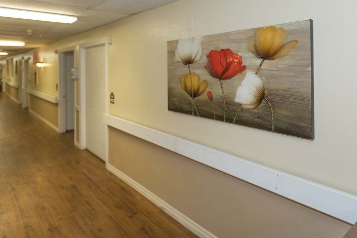 A hallway with wooden flooring and a floral painting on the wall.
