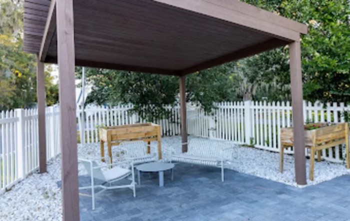 A cozy outdoor patio area with a wooden pergola, surrounded by greenery and featuring comfortable seating.