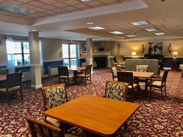 A spacious dining area with multiple tables and chairs, featuring a patterned carpet and ample lighting.