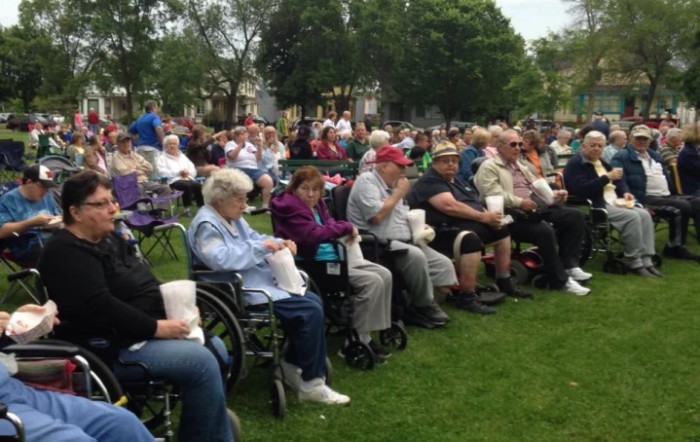 A group of people gathered outdoors, seated on chairs and in wheelchairs, enjoying an event in a park.