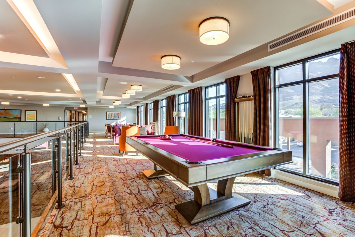 A modern game room featuring a purple pool table with stylish lighting and large windows.