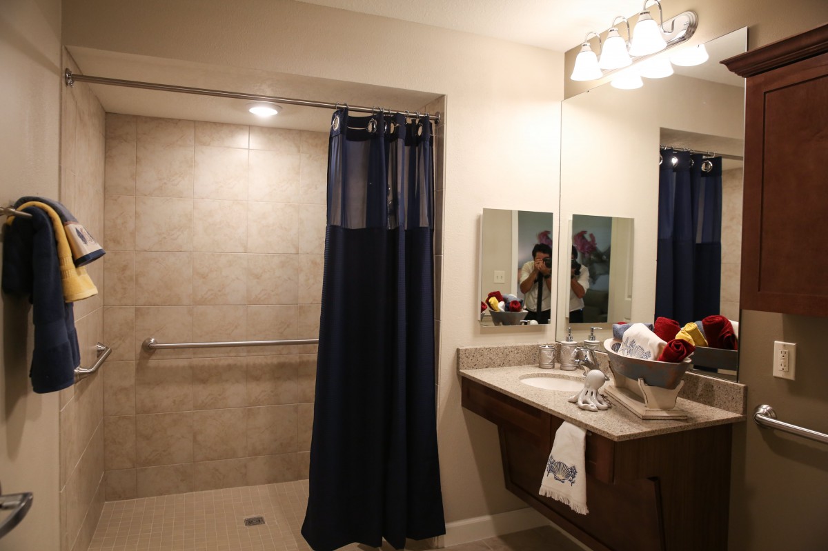 A well-lit bathroom featuring a shower with a navy curtain, a sink area with a mirror, and neatly arranged towels.