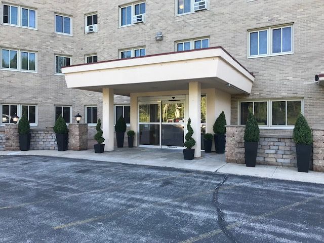 Entrance to a brick apartment building with a covered entryway and decorative plants.