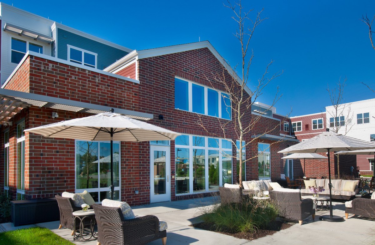 A modern brick building with a spacious patio and outdoor seating on a sunny day.