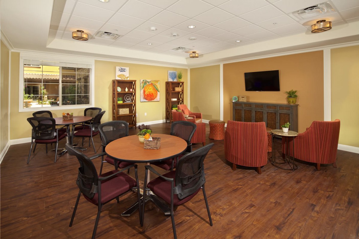 A cozy living room with round tables, comfortable chairs, and a TV on the wall.