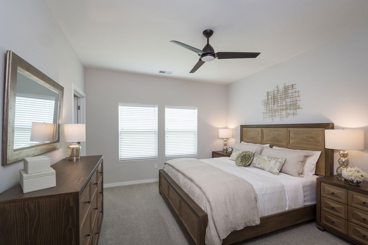A modern bedroom with neutral tones, featuring a large bed, ceiling fan, and stylish decor.