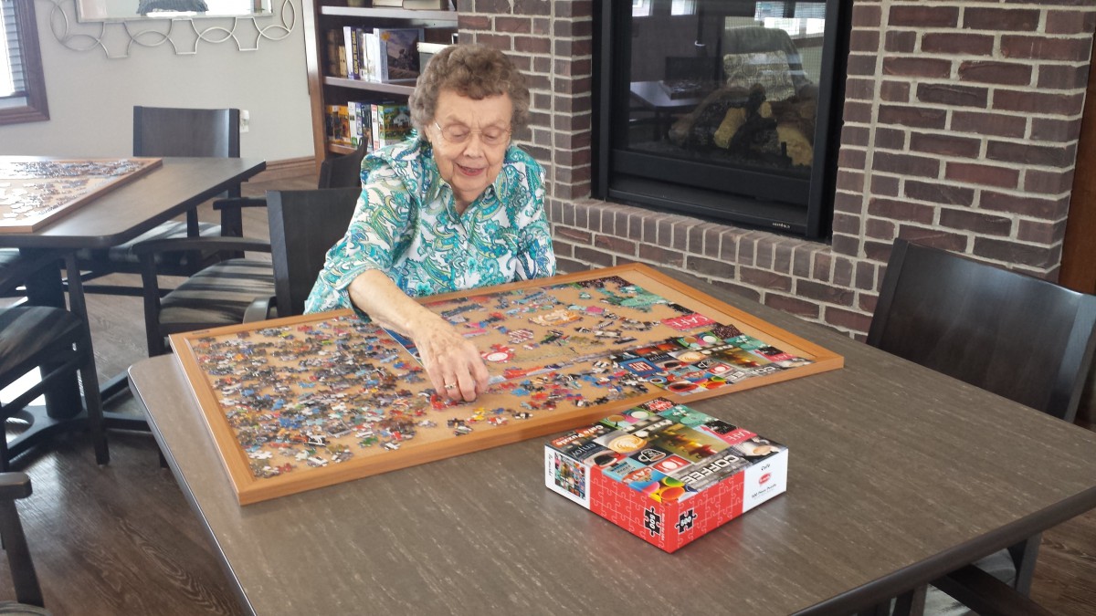 An elderly person happily working on a puzzle at a table indoors.