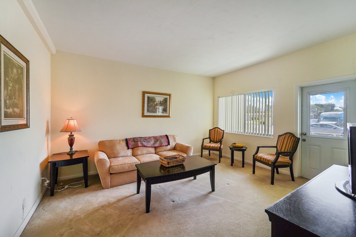 A cozy living room with a sofa, two chairs, and a coffee table, illuminated by a lamp beside the window.