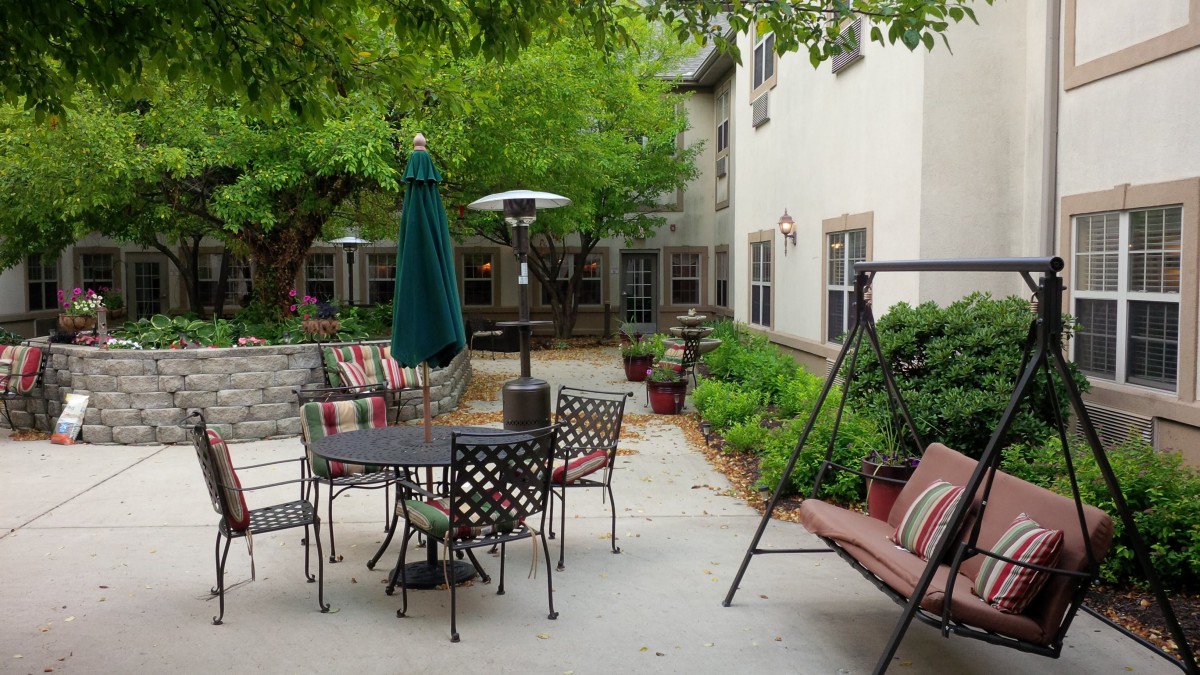 A cozy outdoor patio area with a dining table, chairs, a swing, and lush greenery surrounding the space.
