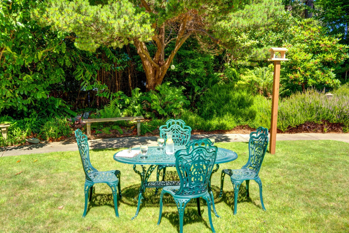 A picturesque garden setting with ornate green patio furniture surrounded by lush greenery.