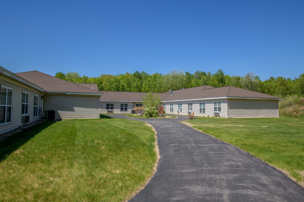 A modern, single-story building surrounded by lush green grass and trees under a bright blue sky.