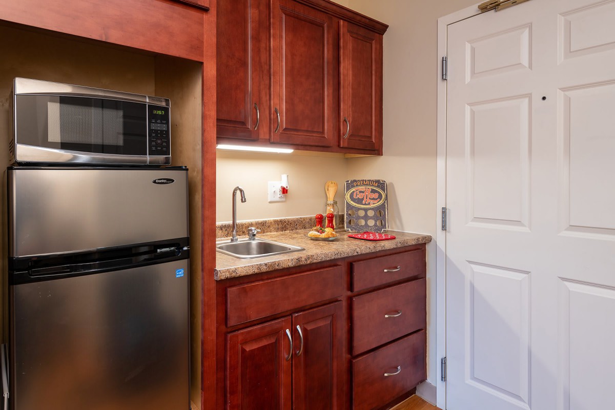 A compact kitchen area featuring a microwave, refrigerator, sink, and wooden cabinets.