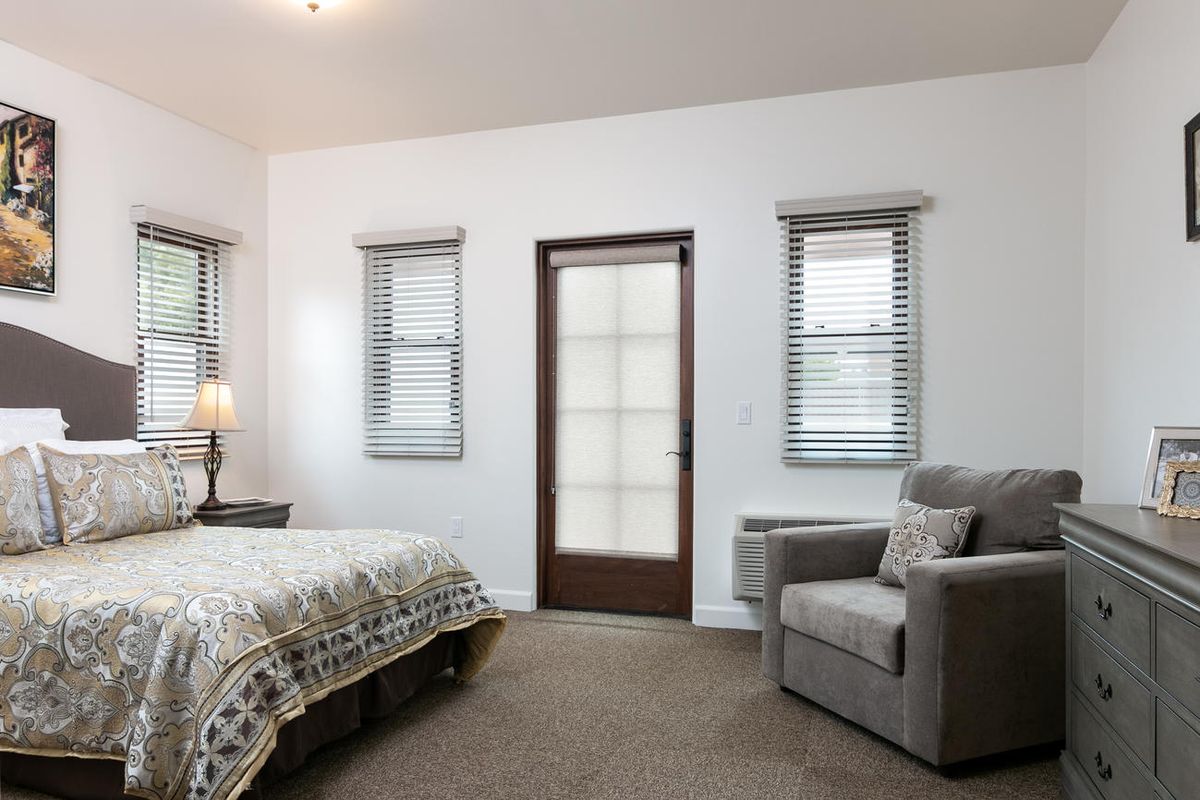 A cozy bedroom featuring a bed, armchair, and a lamp by the window.