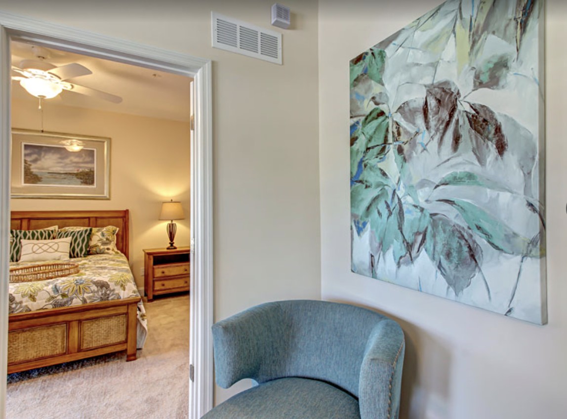 A cozy bedroom with a view through an open doorway, featuring a decorative chair and a large piece of artwork on the wall.