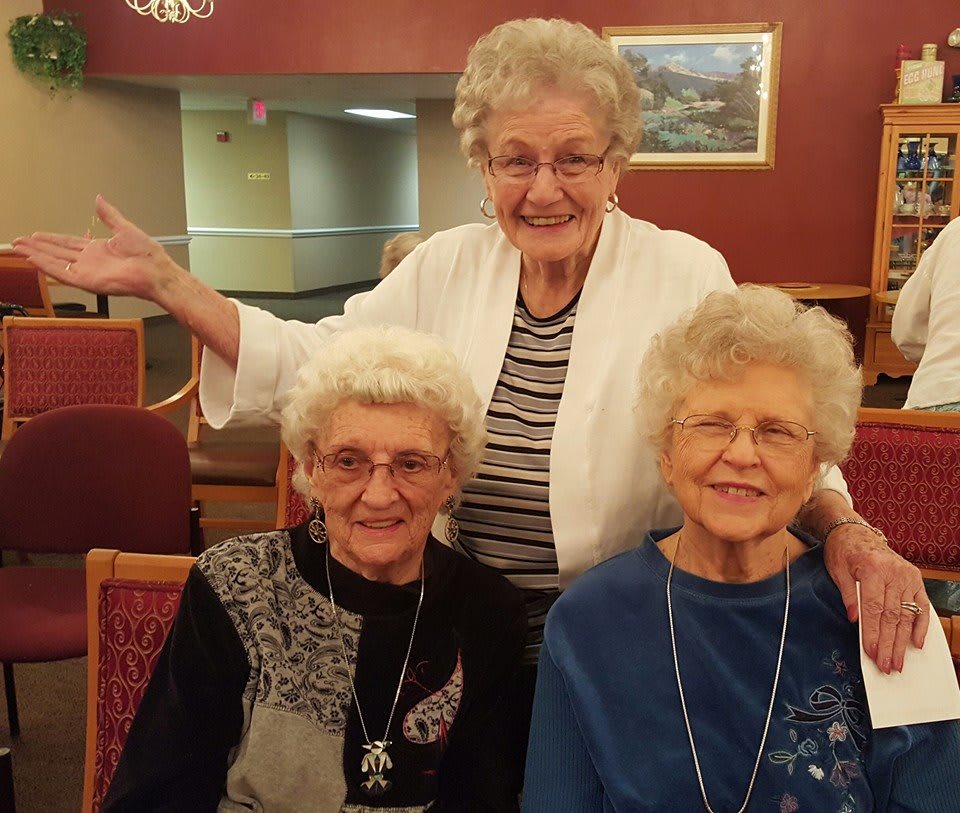 Three elderly women smiling and enjoying each other's company indoors.